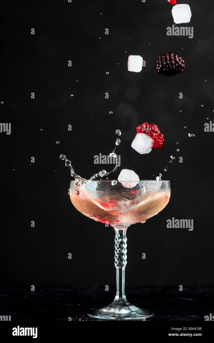 Bicchiere di rosso di cocktail con frutti rossi su sfondo nero, visibili gli schizzi, gocce e la circolazione del liquido Foto Stock