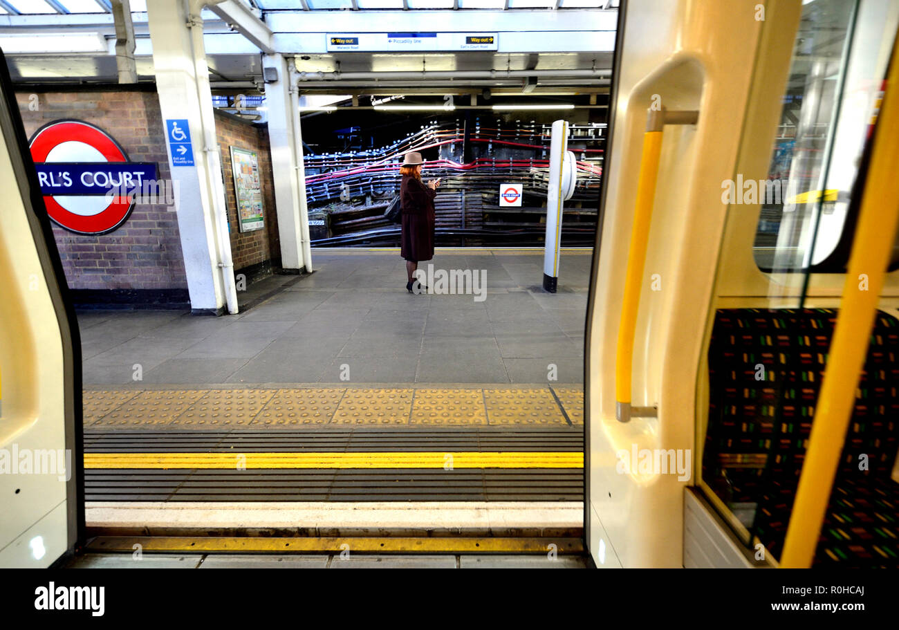 Donna con il suo telefono cellulare sulla piattaforma della stazione della metropolitana di Earl's Court, Londra, Inghilterra, Regno Unito. Foto Stock