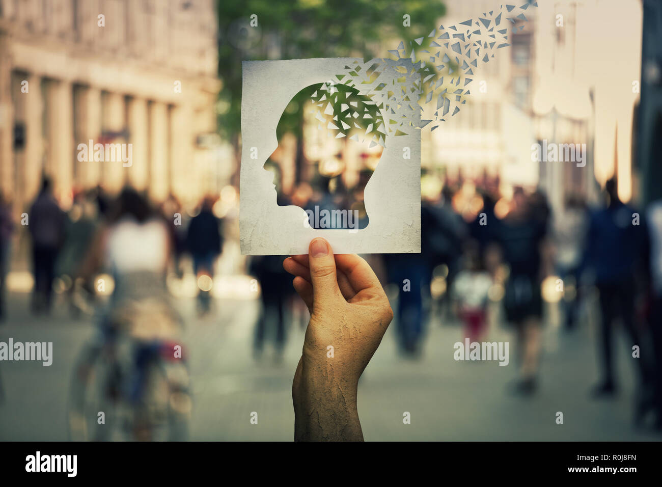 Mano che tiene un foglio di carta con testa umana icona rotta in pezzi su una strada affollata dello sfondo. Concetto di perdita della memoria e demenza malattia. Alzh Foto Stock