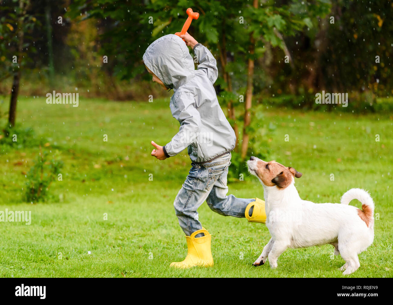 Kid ragazzo indossa impermeabile giocando con il cane sotto la pioggia Foto Stock