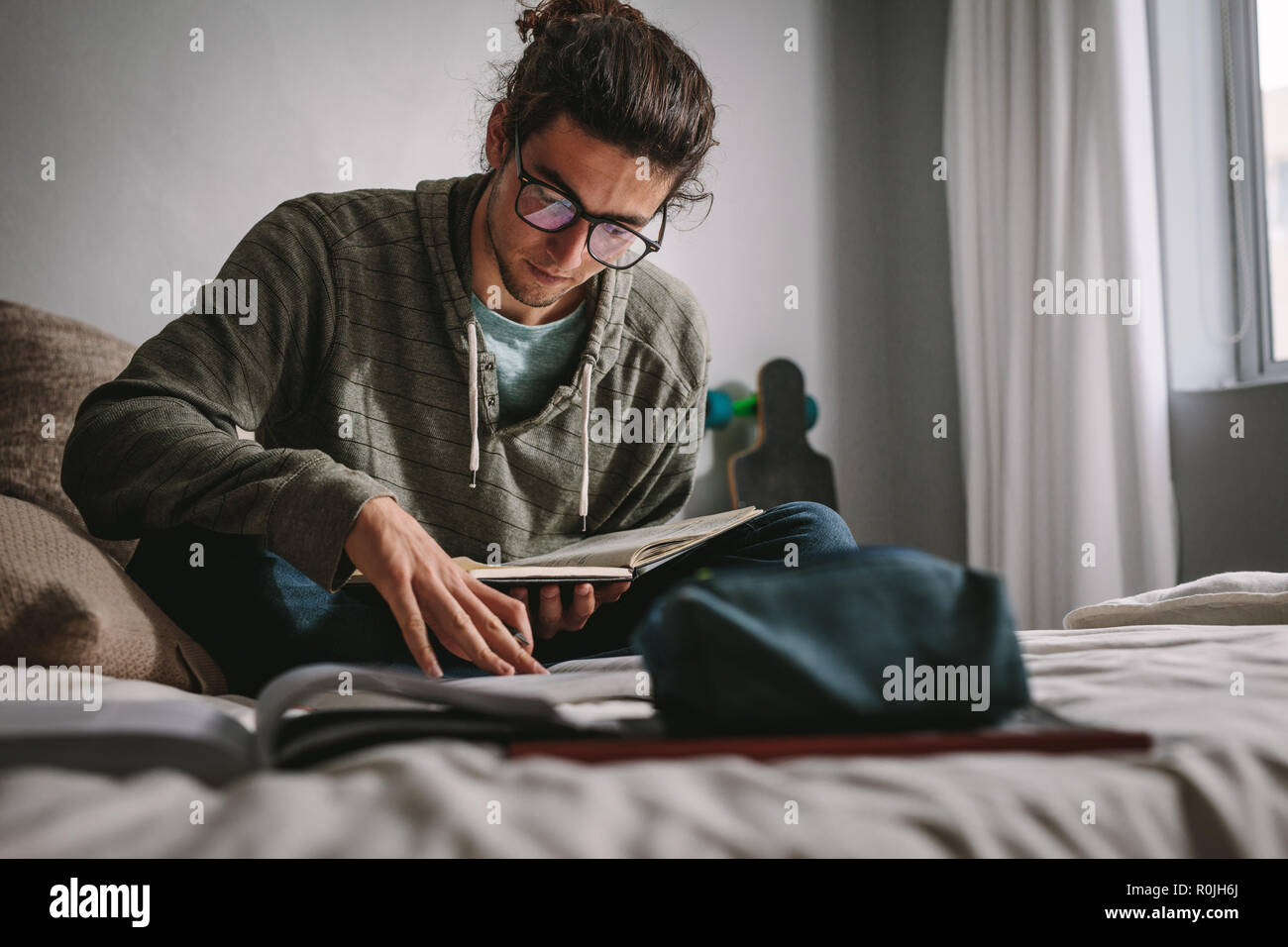 Studente seduto su un letto e studiare con attenzione e concentrazione. Giovane uomo preparazione esame per la lettura di libri. Foto Stock