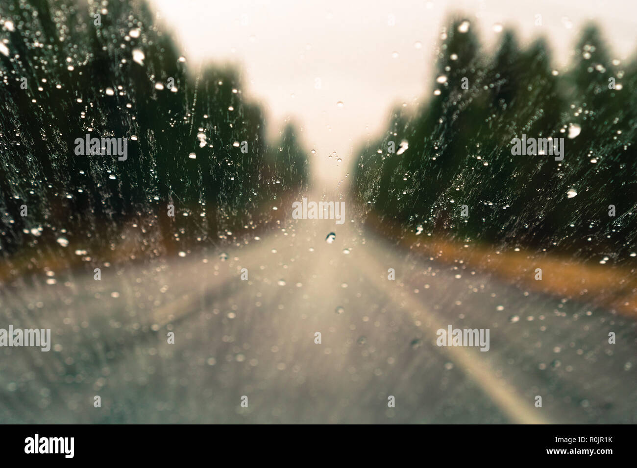 Gocce di pioggia sulla finestra; autostrada sfocata e alberi in background; profondità di campo Foto Stock