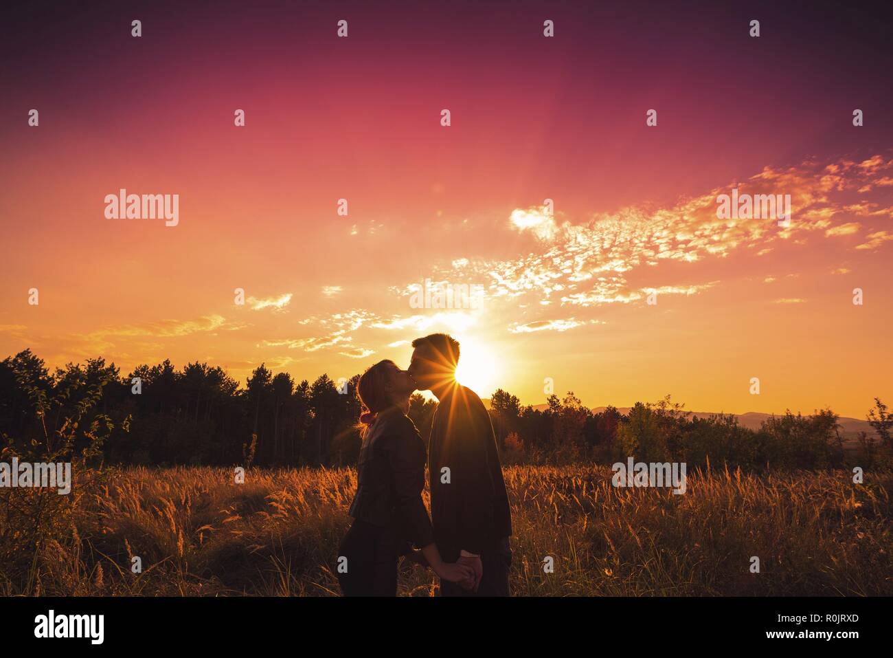 Giovane baciare e tenendo le mani in natura tramonto Foto Stock