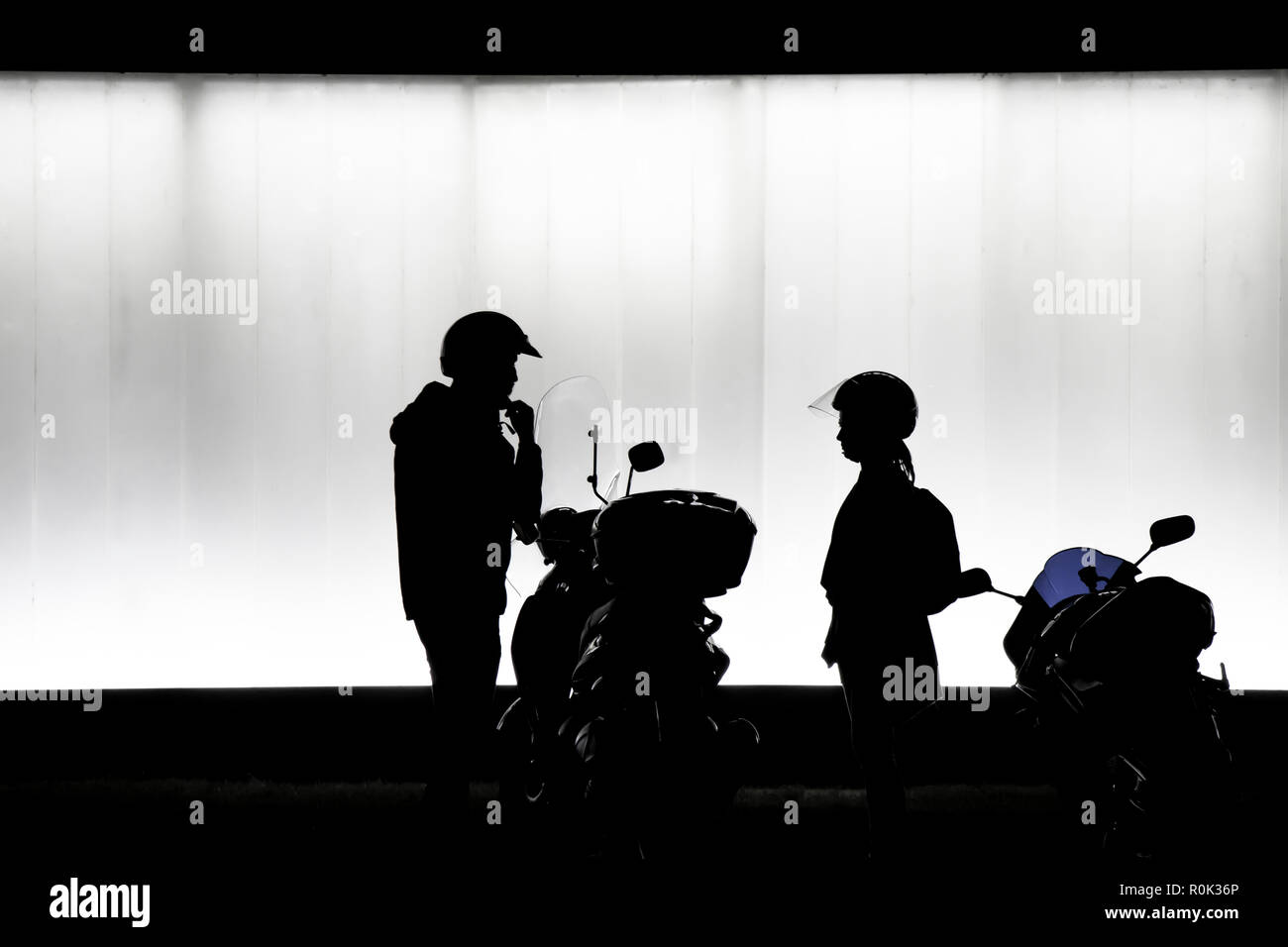 Sfocata la silhouette di un uomo e di una donna di mettere il casco e la preparazione di sedersi su una moto di fronte all edificio moderno nella notte in bianco e nero Foto Stock