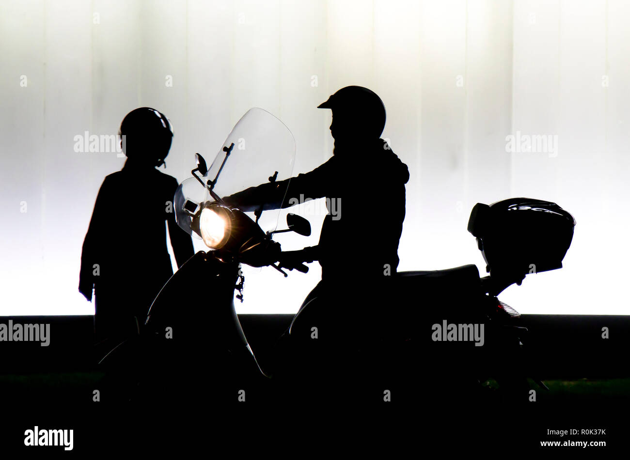 Sfocata silhouette di due persone in partenza su una moto di fronte all edificio moderno in sella a una motocicletta con faro su nella notte in bianco e nero e w Foto Stock