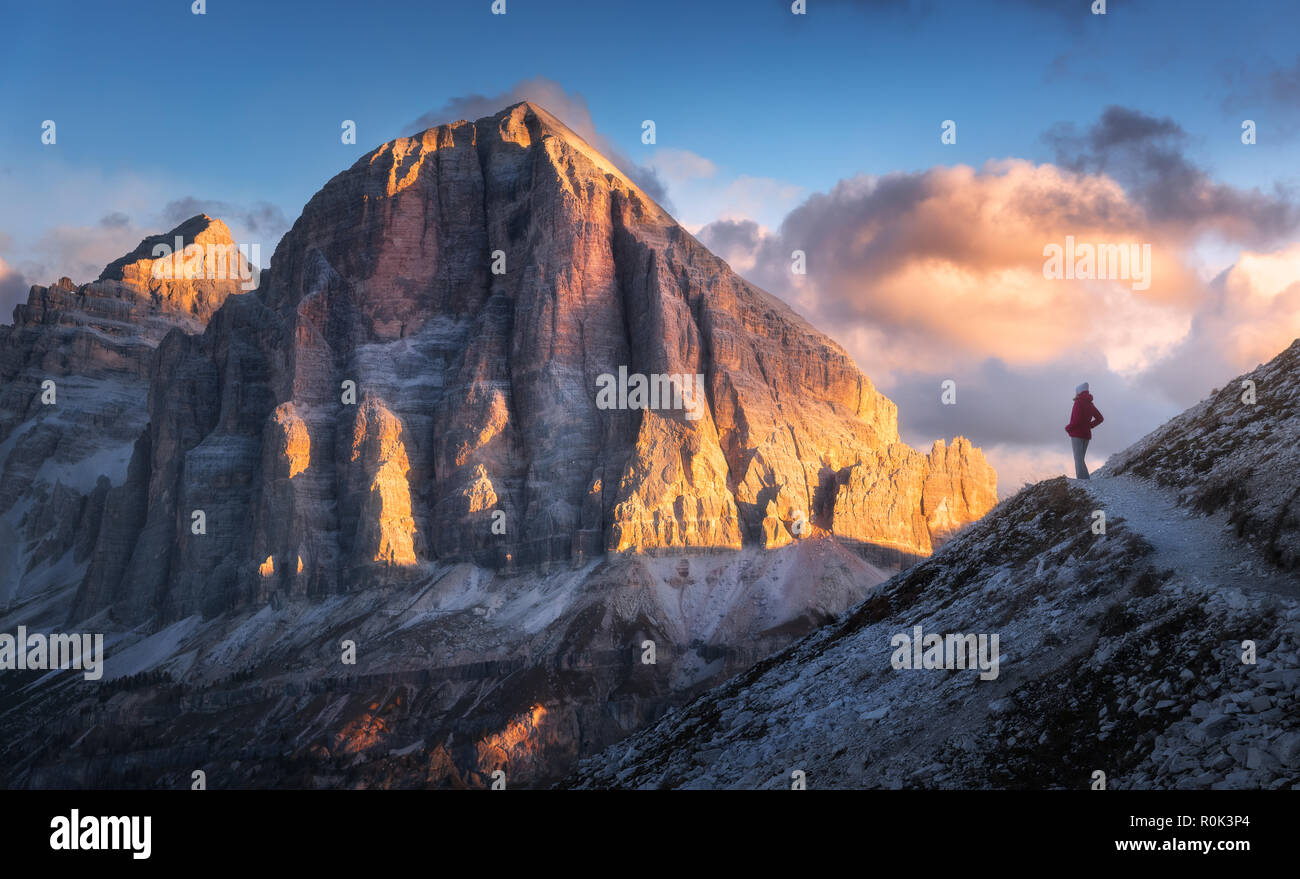 Giovane donna sul sentiero a guardare verso l'alto picco di montagna al Tramonto nelle Dolomiti, Italia. Paesaggio autunnale con la ragazza, percorso, rocce, cielo con nuvole a colo Foto Stock