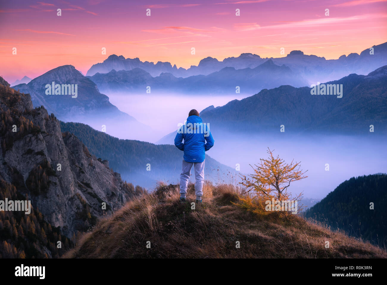 Uomo sportivo sul picco di montagna cercando sulla valle di montagna con nuvole basse al tramonto colorato in autunno nelle Dolomiti. Paesaggio con traveler, foggy h Foto Stock