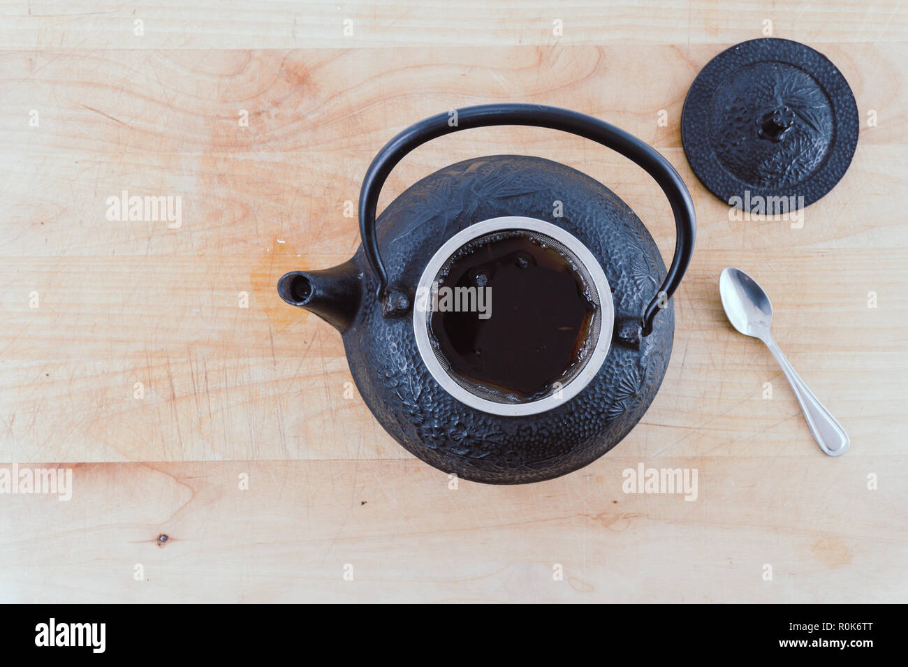 Vista dall'alto di ghisa nera teiera piena di tè caldo con un cucchiaio su una sbiadita tavolo in legno o il vassoio. Instagram look. Hygge. Accogliente. Foto Stock