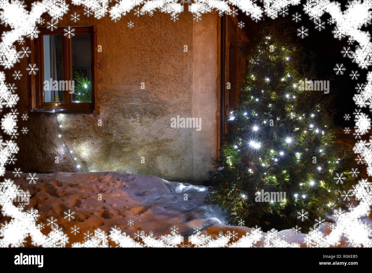 Decorate albero di Natale brilla nella natura innevata accanto alla vecchia casa. Accesa X-mas illuminazione ad albero nel giardino d'inverno. Foto Stock