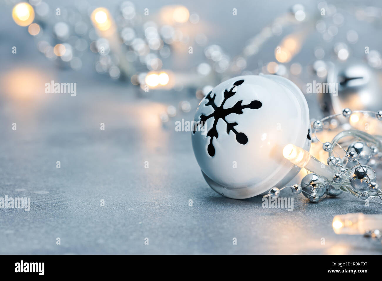 Jingle Bell e incandescente ghirlanda di Natale luci sul grigio Sfondo frosty. sfocata vista macro Foto Stock
