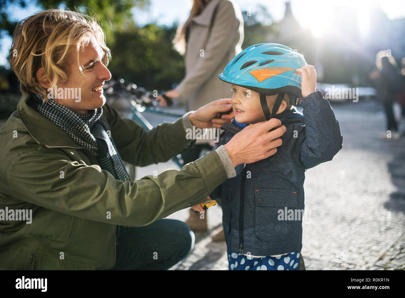 Un giovane padre mettendo su un casco sul suo figlio toddler la testa all'aperto in città. Foto Stock