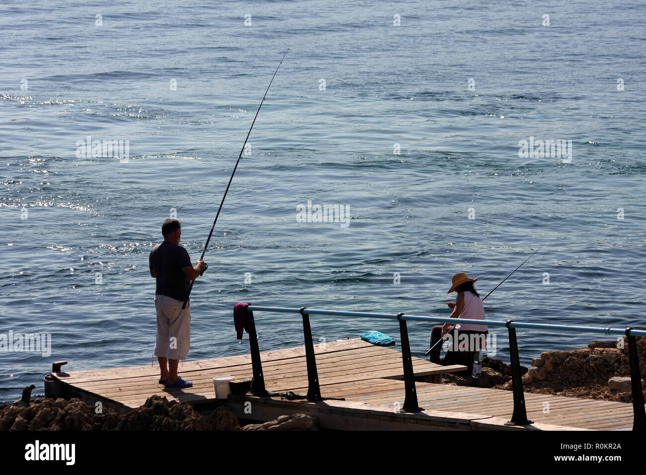 L'uomo pesca dal molo con la donna guardando in vacanza a Maiorca. Foto Stock