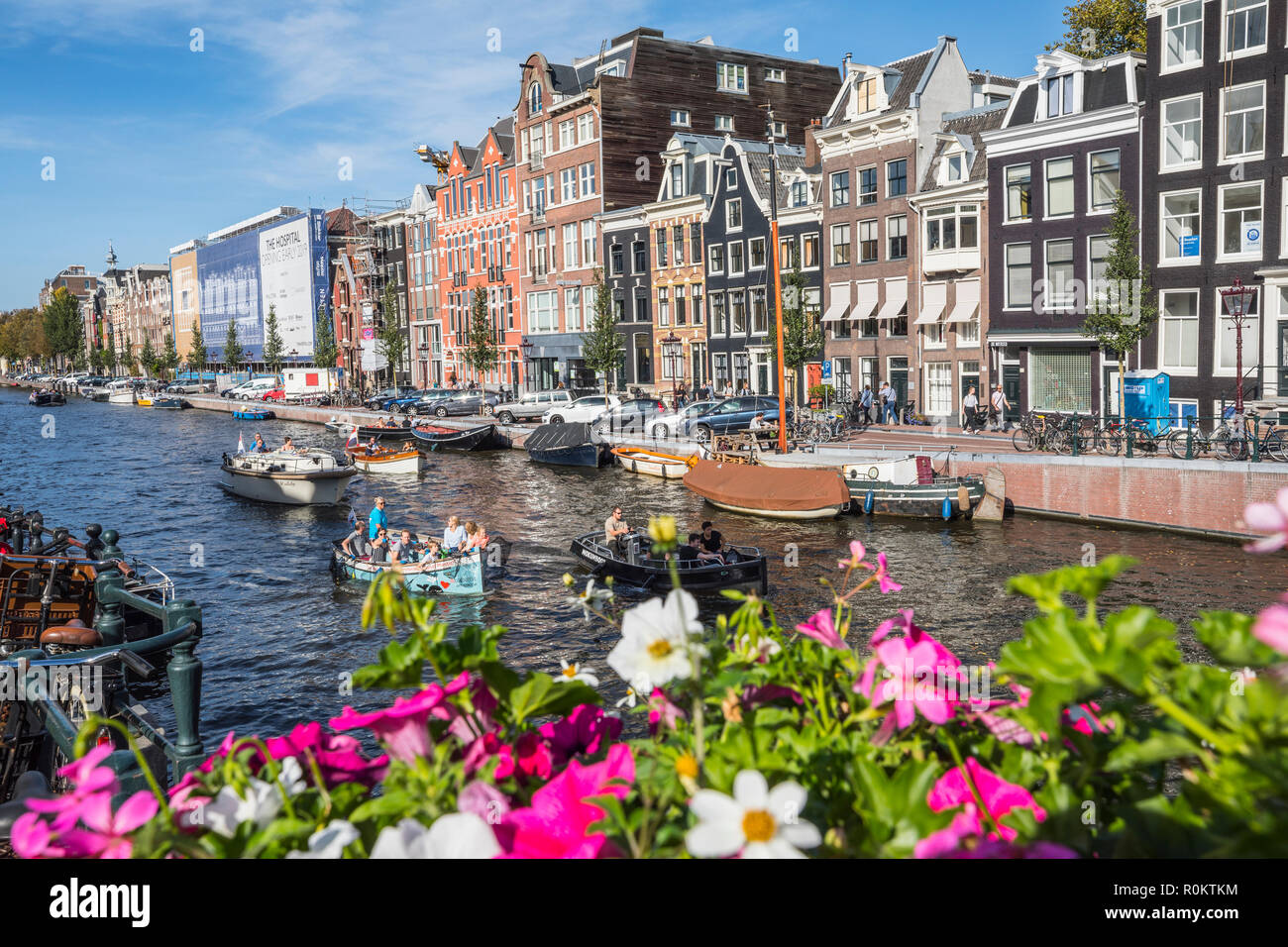 Vista sul canale di Amsterdam con imbarcazioni turistiche oltre i fiori colorati sul ponte Foto Stock