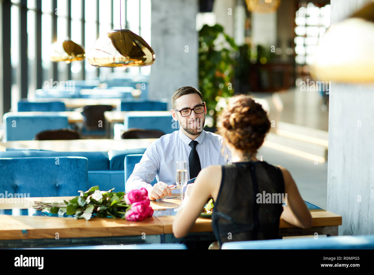 Elegante uomo che parla di giovane donna in abito nero dalla cena romantica nel ristorante Foto Stock