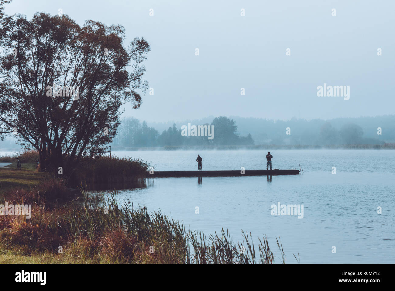 Due pescatori in piedi sulla riva del lago nella mattinata nebbiosa Foto Stock