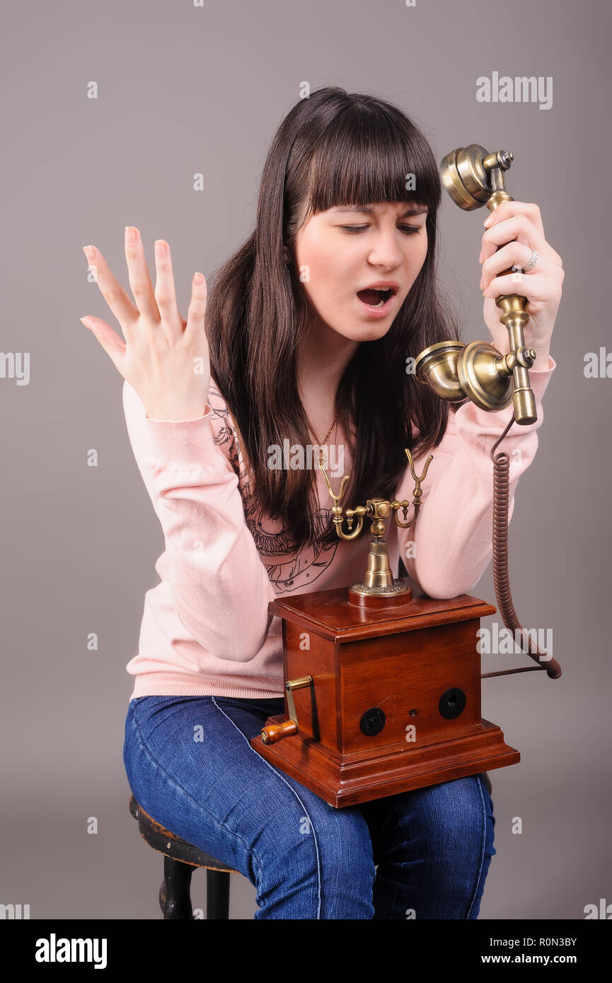 Giovane donna attraente grida nel telefono vintage su sfondo grigio Foto Stock