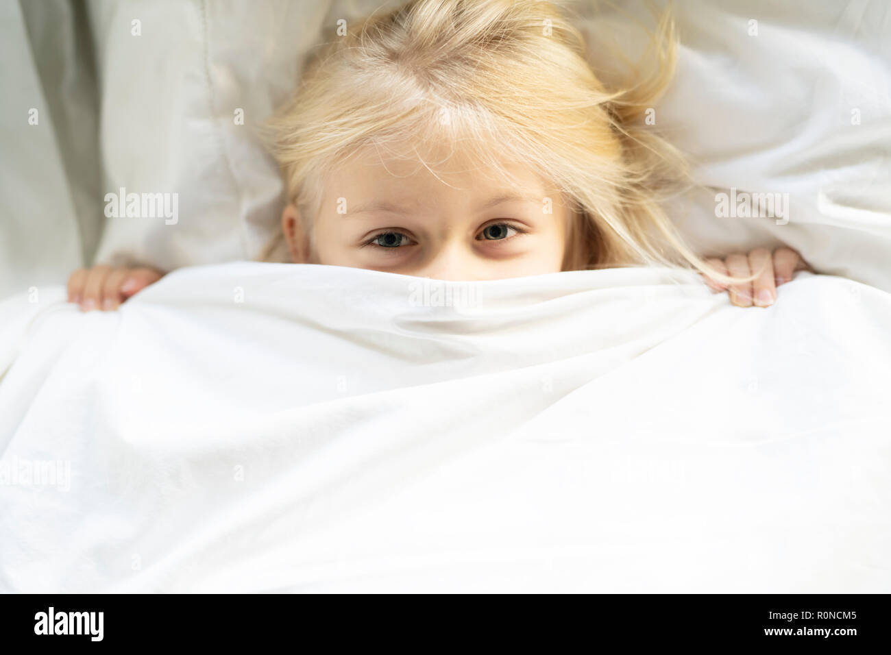Una bambina nel letto al di sotto dei coperchi Foto Stock