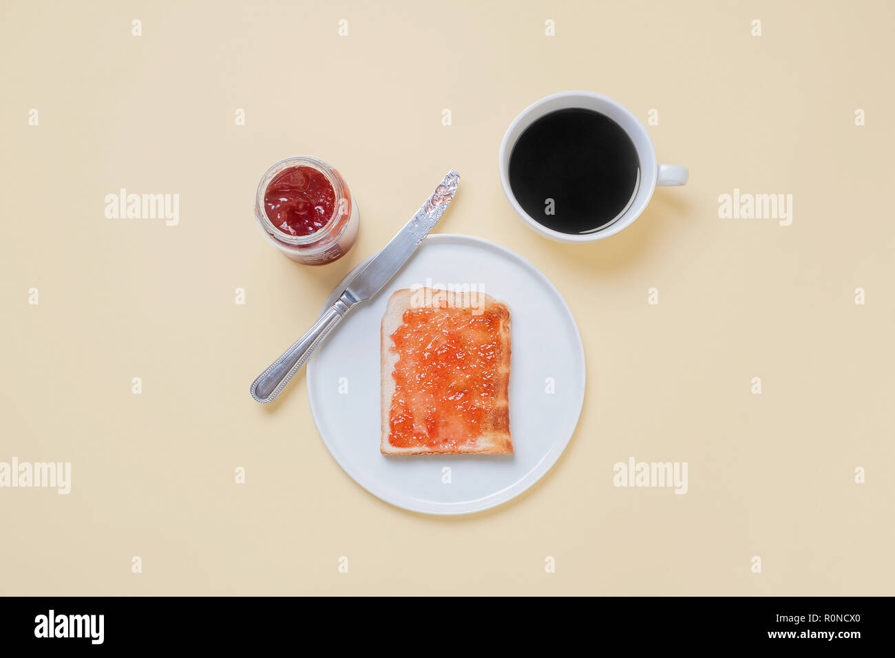 Vista superiore del toast con marmellata di fragole confettura su una piastra bianca con la lama di un coltello, caffè e un vasetto di conserva su un vintage tan sfondo con spazio di copia Foto Stock