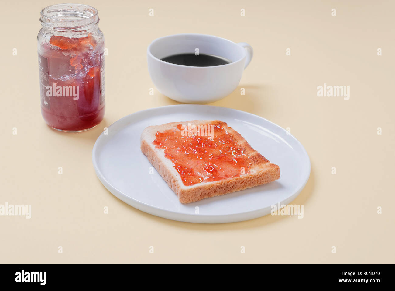 Fetta di pane tostato con marmellata di fragola jelly su una piastra bianca con una tazza di caffè e un barattolo di conserva su un vintage tan sfondo con spazio di copia Foto Stock