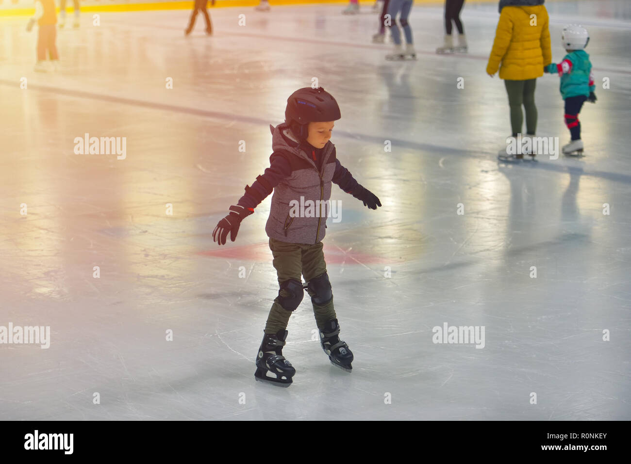 Adorable little boy in abbigliamento invernale con protezioni a pattinare  sulla pista di pattinaggio su ghiaccio Foto stock - Alamy