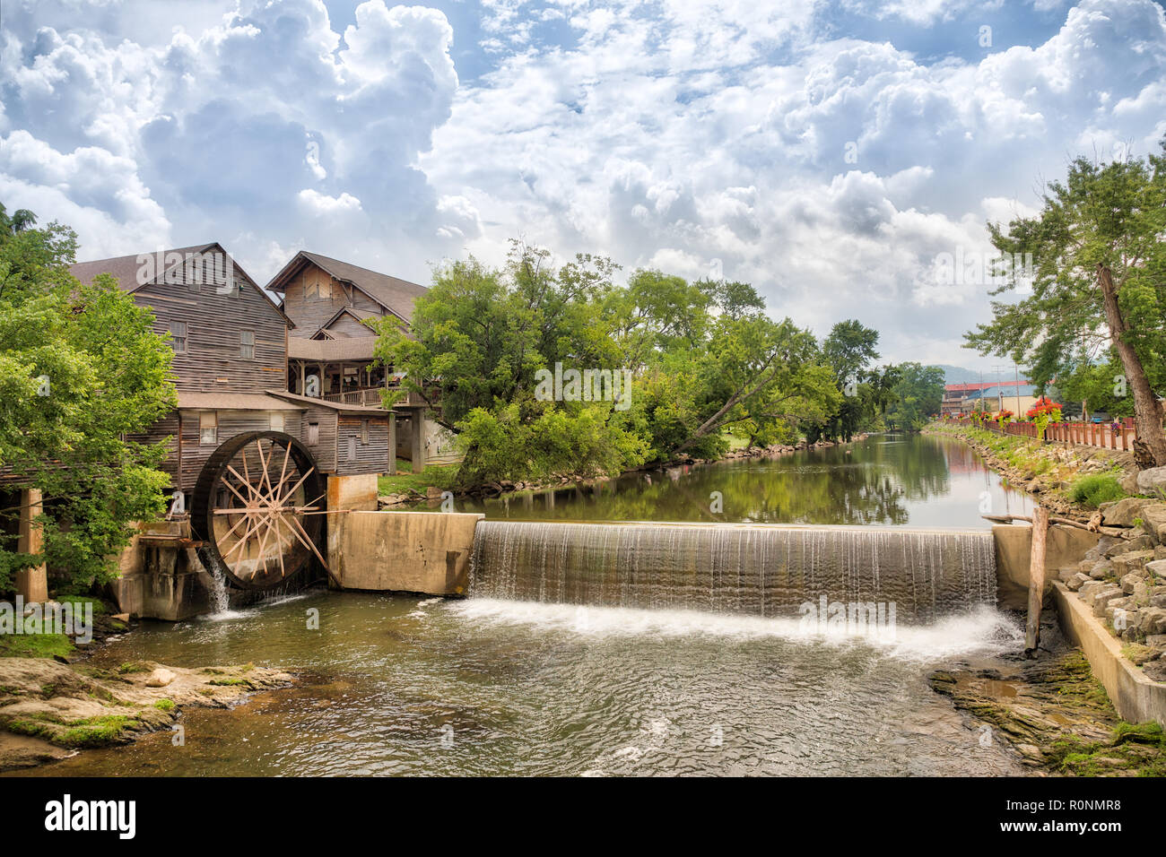 Foto orizzontale di un fiume e il vecchio mulino con il cielo blu con nuvole e gli alberi che riflette nell'acqua. Foto Stock