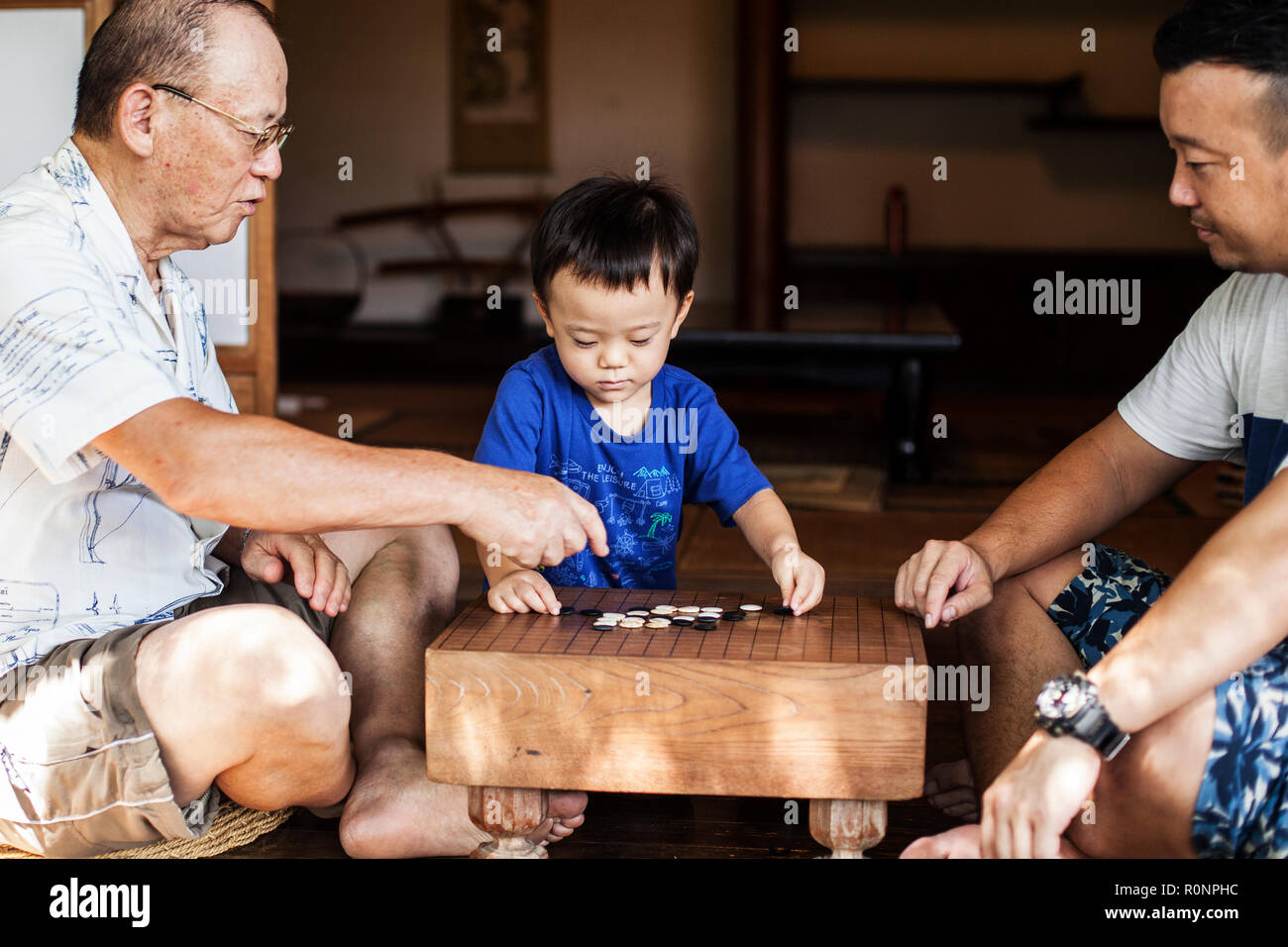 Due uomini giapponesi e piccolo ragazzo seduto sul pavimento sul portico di casa tradizionale giapponese, riproduzione di andare. Foto Stock