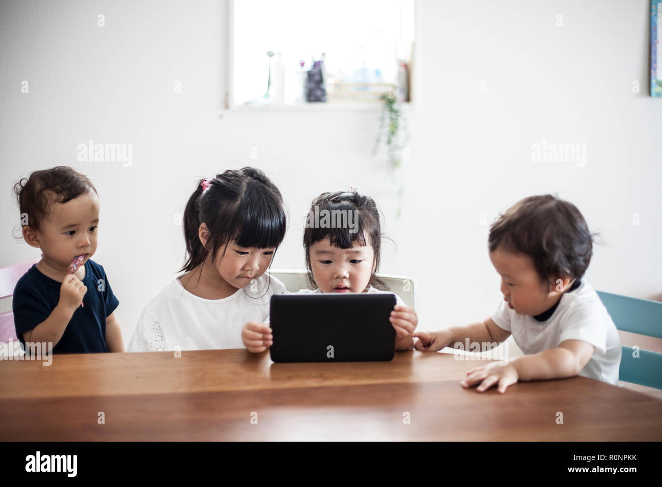 Quattro giovani giapponesi bambini seduti a un tavolo, guardando a tavoletta digitale. Foto Stock