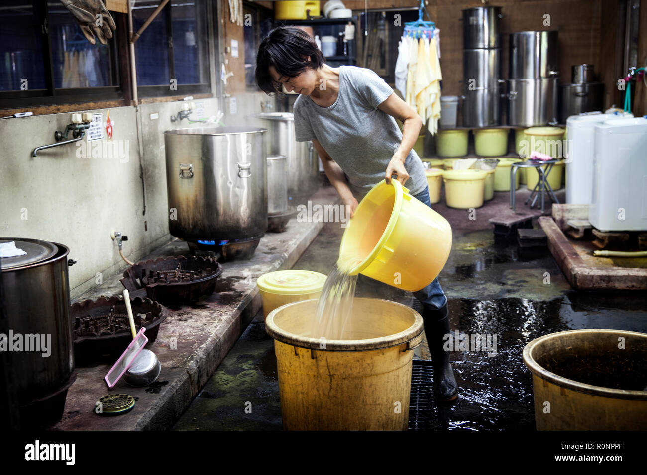 Donna Giapponese lavora in un impianto tessile officina di colorante, versando acqua calda in giallo secchielli in plastica. Foto Stock