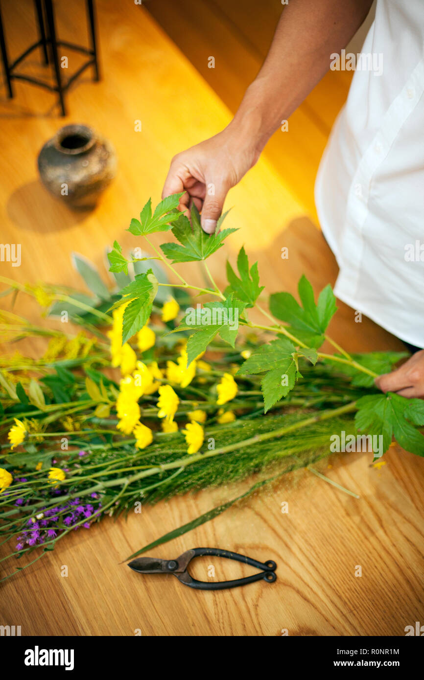 Persona in piedi in galleria fiori, lavorando sulla disposizione di Ikebana con foglie di colore giallo e viola fiore. Foto Stock