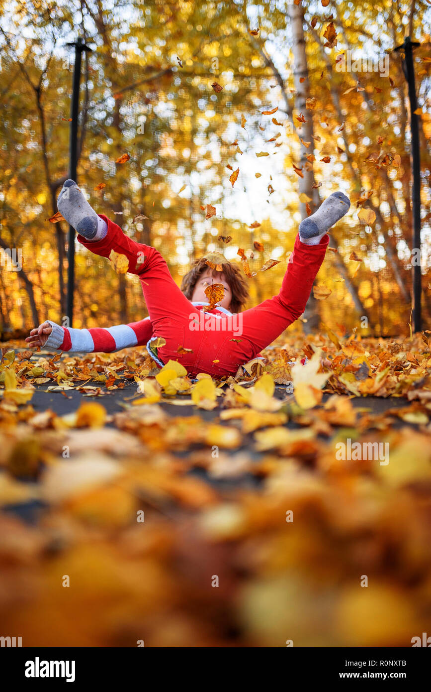 Ragazzo saltando su un trampolino coperto di foglie di autunno, Stati Uniti Foto Stock