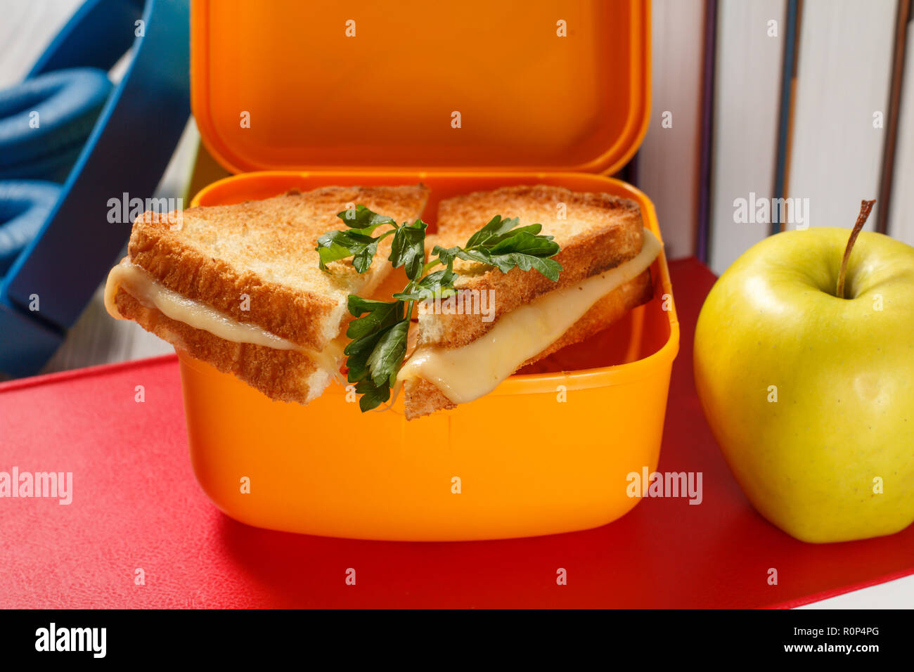 Giallo casella a sandwich con le fette biscottate di pane, formaggio e prezzemolo verde, verde mela, cuffie e rigida libri sullo sfondo. Rottura della scuola Foto Stock