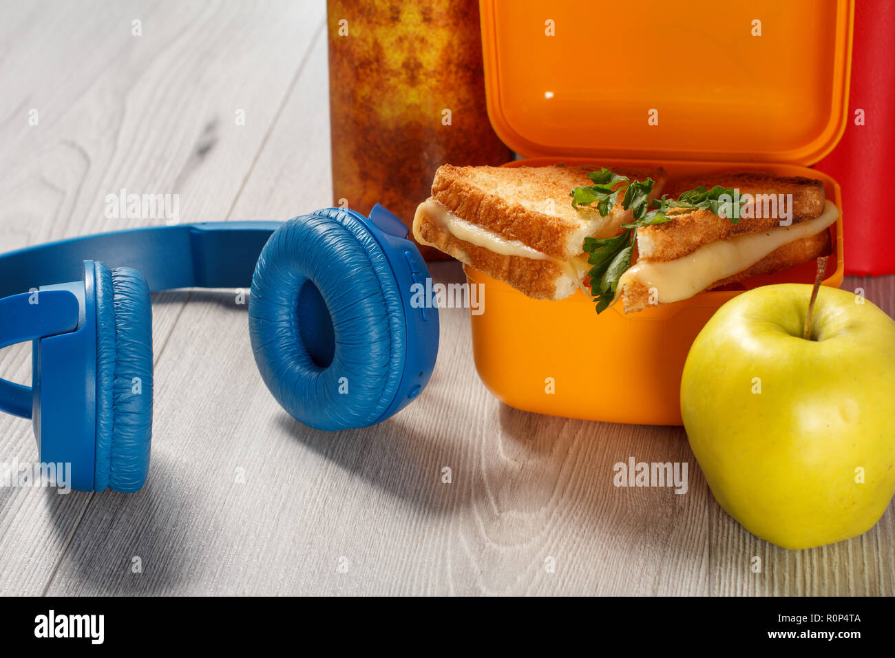 Giallo casella a sandwich con le fette biscottate di pane, formaggio e prezzemolo verde, verde mela, cuffie e rigida libri sullo sfondo. Rottura della scuola Foto Stock