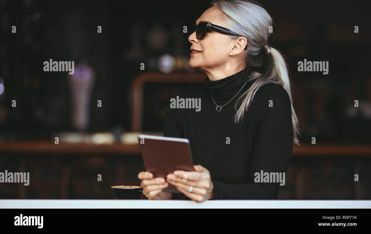 Bella senior imprenditrice seduti ad un ristorante con tavoletta digitale. Donna matura in un coffee shop con tablet pc. Foto Stock