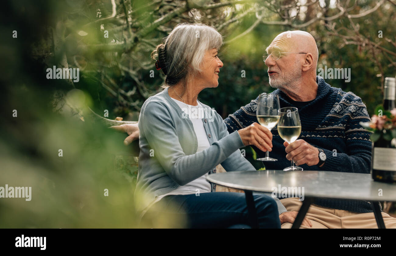 Il vecchio uomo e donna di trascorrere del tempo insieme a bere vino. Vecchia coppia seduti insieme in un giardino azienda bicchieri da vino guardando ogni altro. Foto Stock
