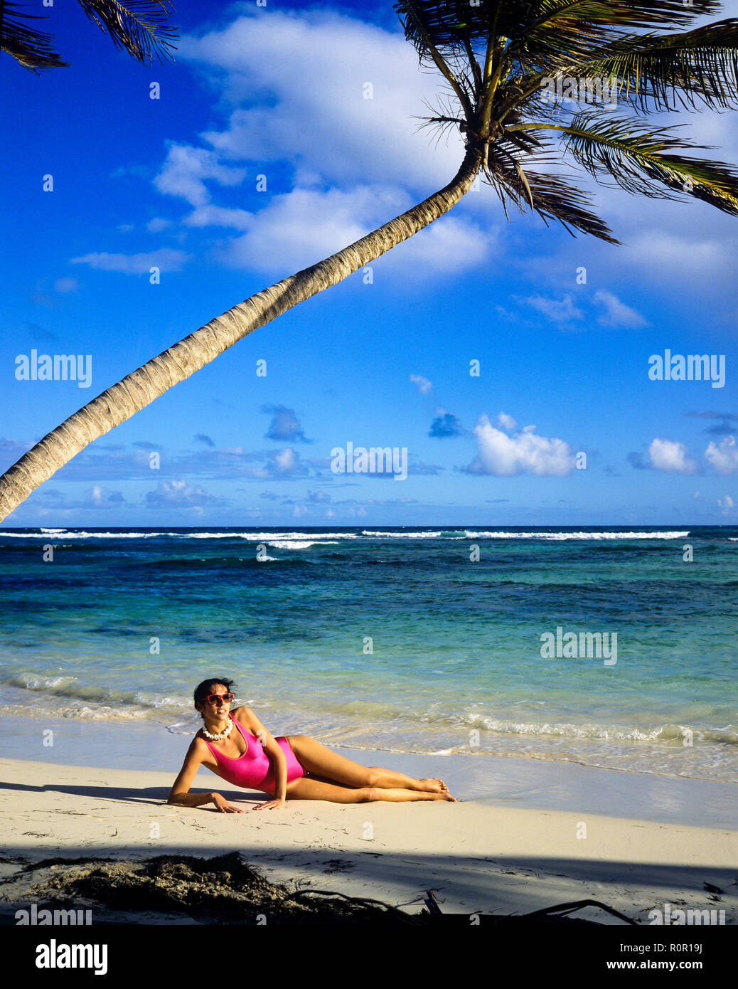 Giovane donna con rosa costume da bagno a prendere il sole sulla spiaggia tropicale, Palm tree, il mare dei Caraibi, Guadalupa, French West Indies, Foto Stock
