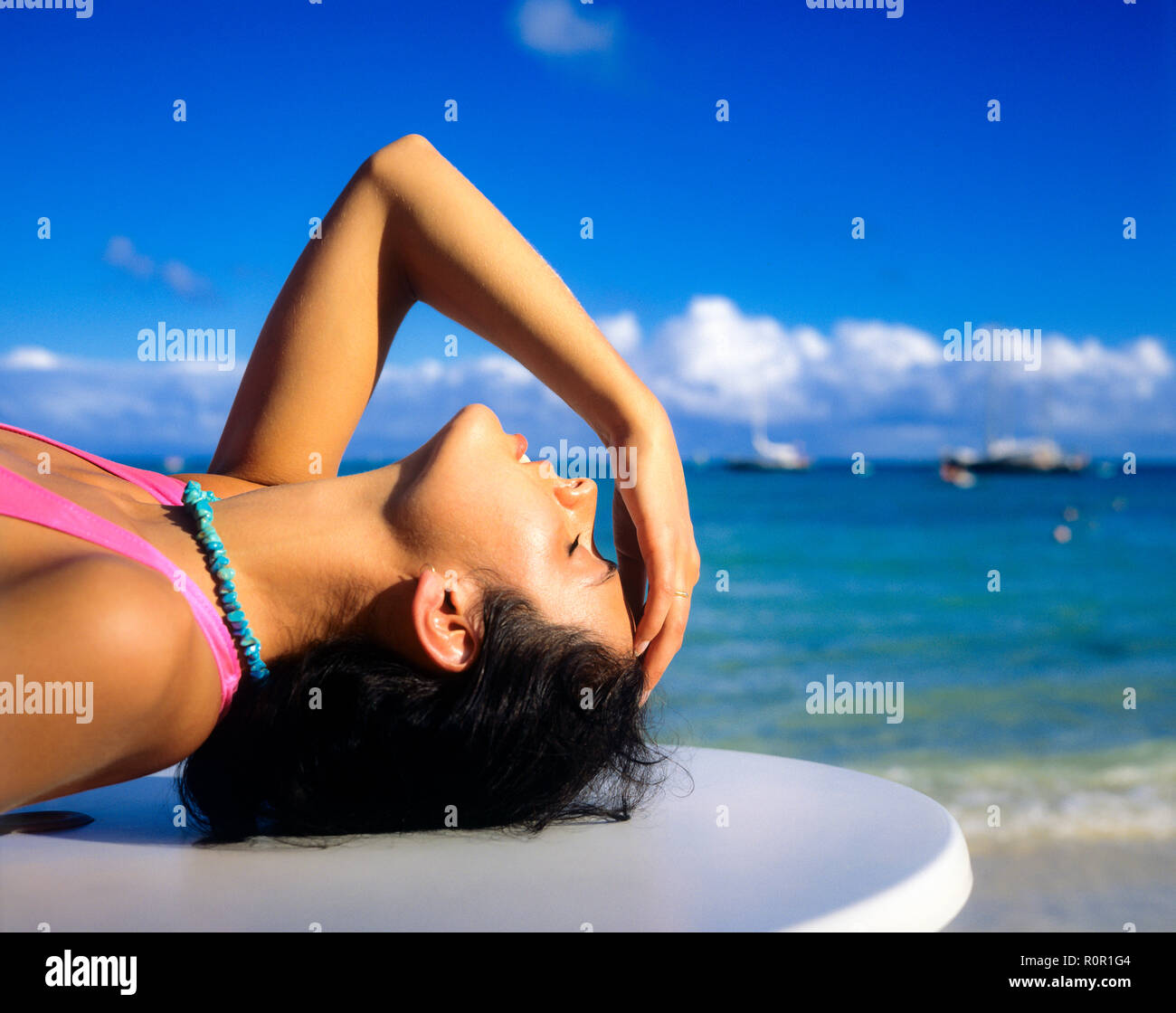 Ritratto di giovane donna a prendere il sole a occhi chiusi, tenendo la testa con la mano, il mare dei Caraibi, Guadalupa, French West Indies, Foto Stock