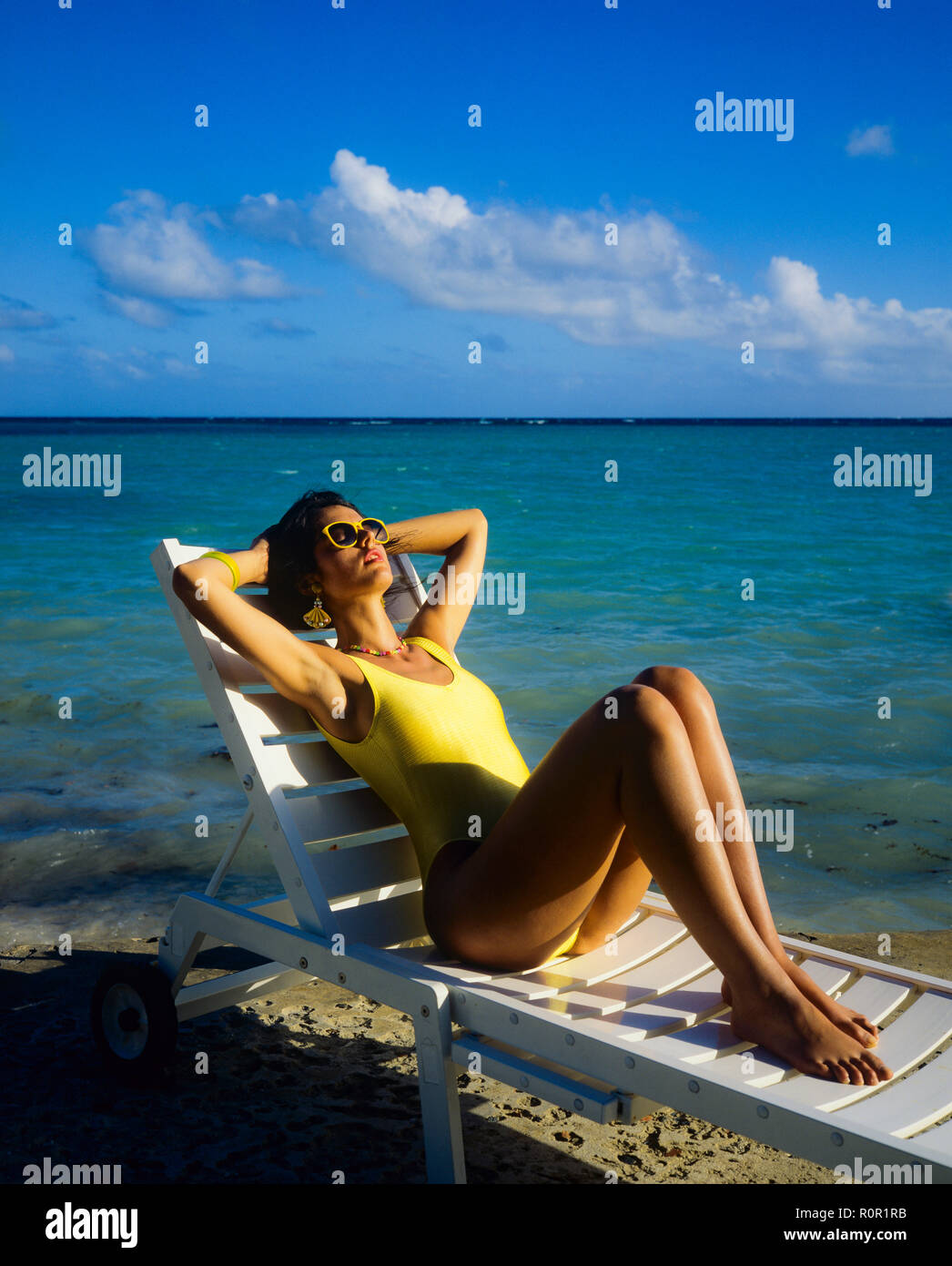 Giovane donna con il costume da bagno giallo sole e rilassarsi in prendisole, spiaggia tropicale, il mare dei Caraibi, Guadalupa, French West Indies, Foto Stock