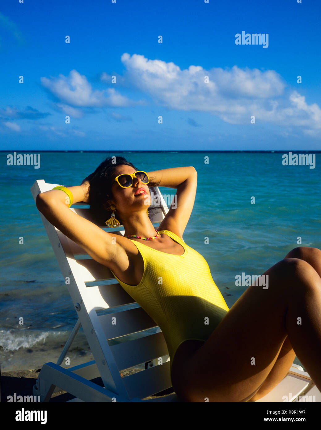 Giovane donna con il costume da bagno giallo sole e rilassarsi in prendisole, spiaggia tropicale, il mare dei Caraibi, Guadalupa, French West Indies, Foto Stock