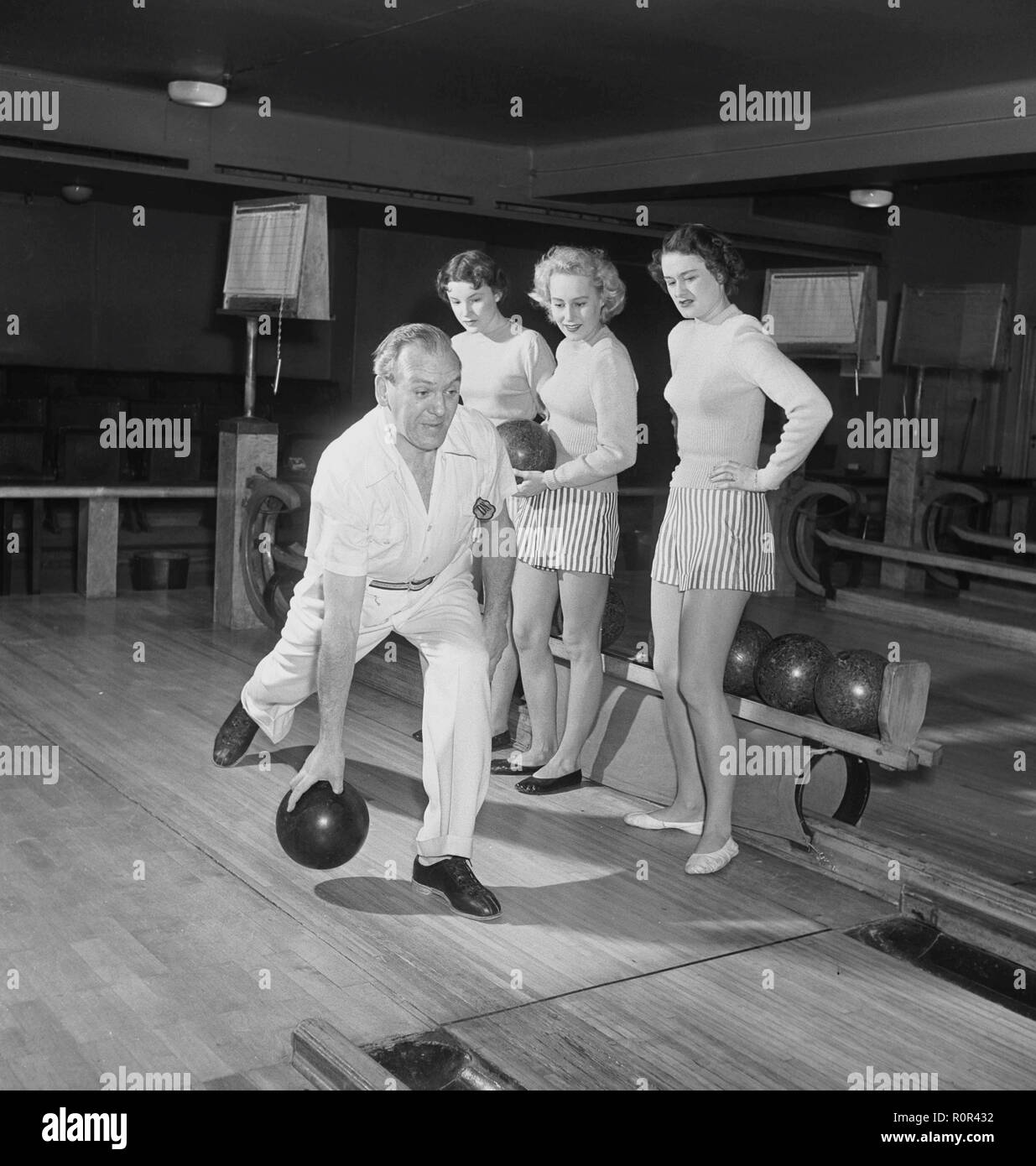 Bowling nel 1950s. Un uomo sta lanciando la palla da bowling e tre giovani donne sono in piedi accanto e guardare, sono vestite di corte gonne a strisce e jumper. Le tre ragazze sono tutte attrici teatrali: Ingrid Björk, UllaCarin Rydén e Brita Ulfberg. Gli spettacoli di Ewert Ekström li insegnano a giocare a bowling. Era un giocatore professionista di bowler nel 1930s ed è a questo tempo un istruttore ed un proprietario del randello di bowling. 1950 Svezia Foto Kristoffersson Ref AY36-3 Foto Stock