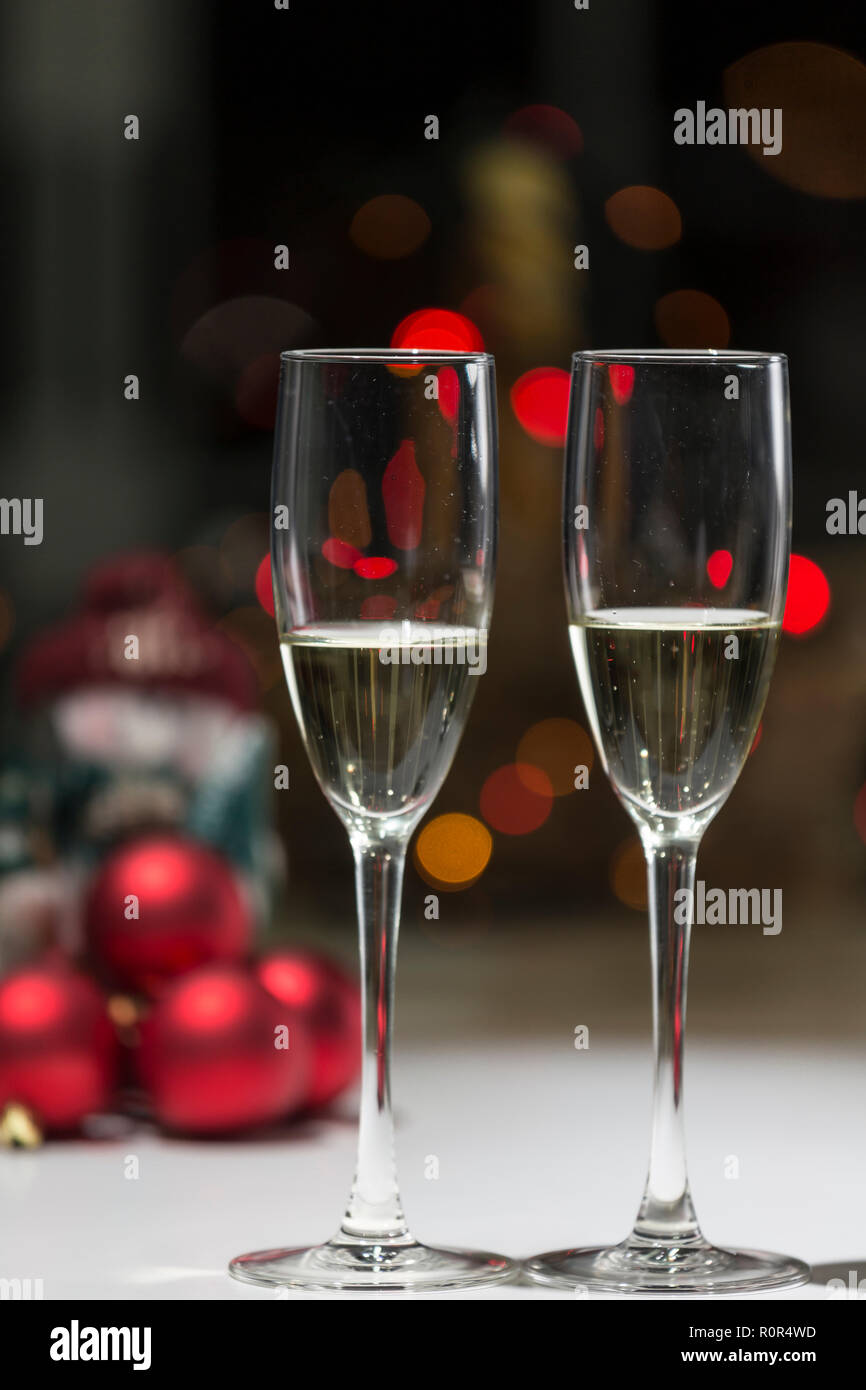 Due bicchieri di champagne, sullo sfondo di una atmosfera natalizia nei toni del rosso e del calore di casa Foto Stock