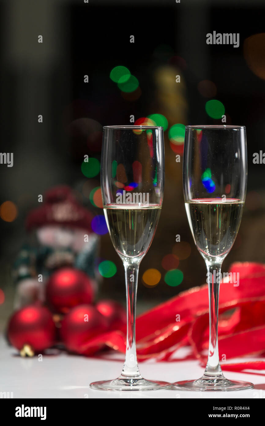 Due bicchieri di champagne, sullo sfondo di una atmosfera natalizia nei toni del rosso e del calore di casa Foto Stock