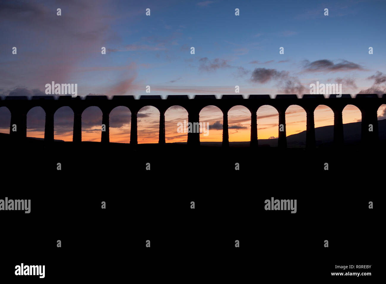Un GB di merci su rotaie di treni merci pietra portante facendo una silhouette incrocio viadotto Ribblehead al tramonto Foto Stock