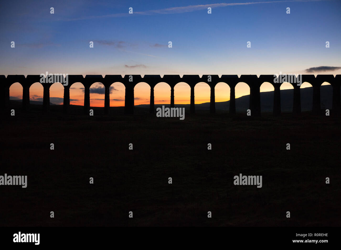 Un GB di merci su rotaie di treni merci pietra portante facendo una silhouette incrocio viadotto Ribblehead al tramonto Foto Stock