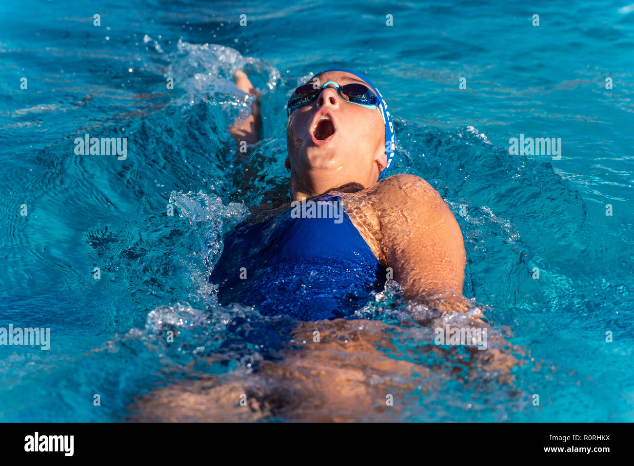 Femmina competitivo nuotatore prendendo grande soffio di aria come ella velocità verso la linea di finitura durante la gara di dorso. Foto Stock