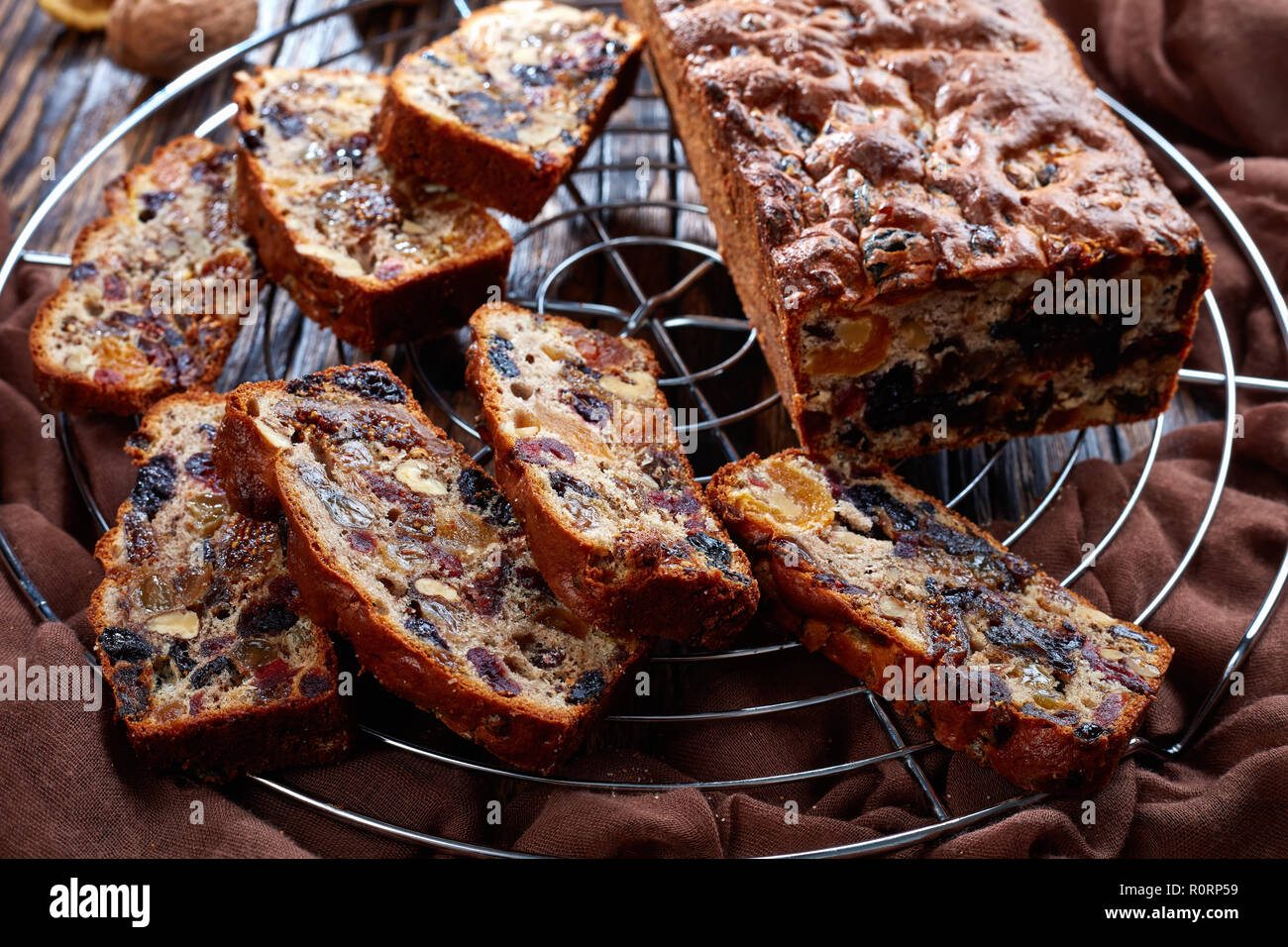 Pane appena sfornato e la frutta secca ricca torta su un filo cake stand con panno marrone, bastoncini di cannella, albicocche secche e data la frutta in una tavola in legno rustico, Foto Stock