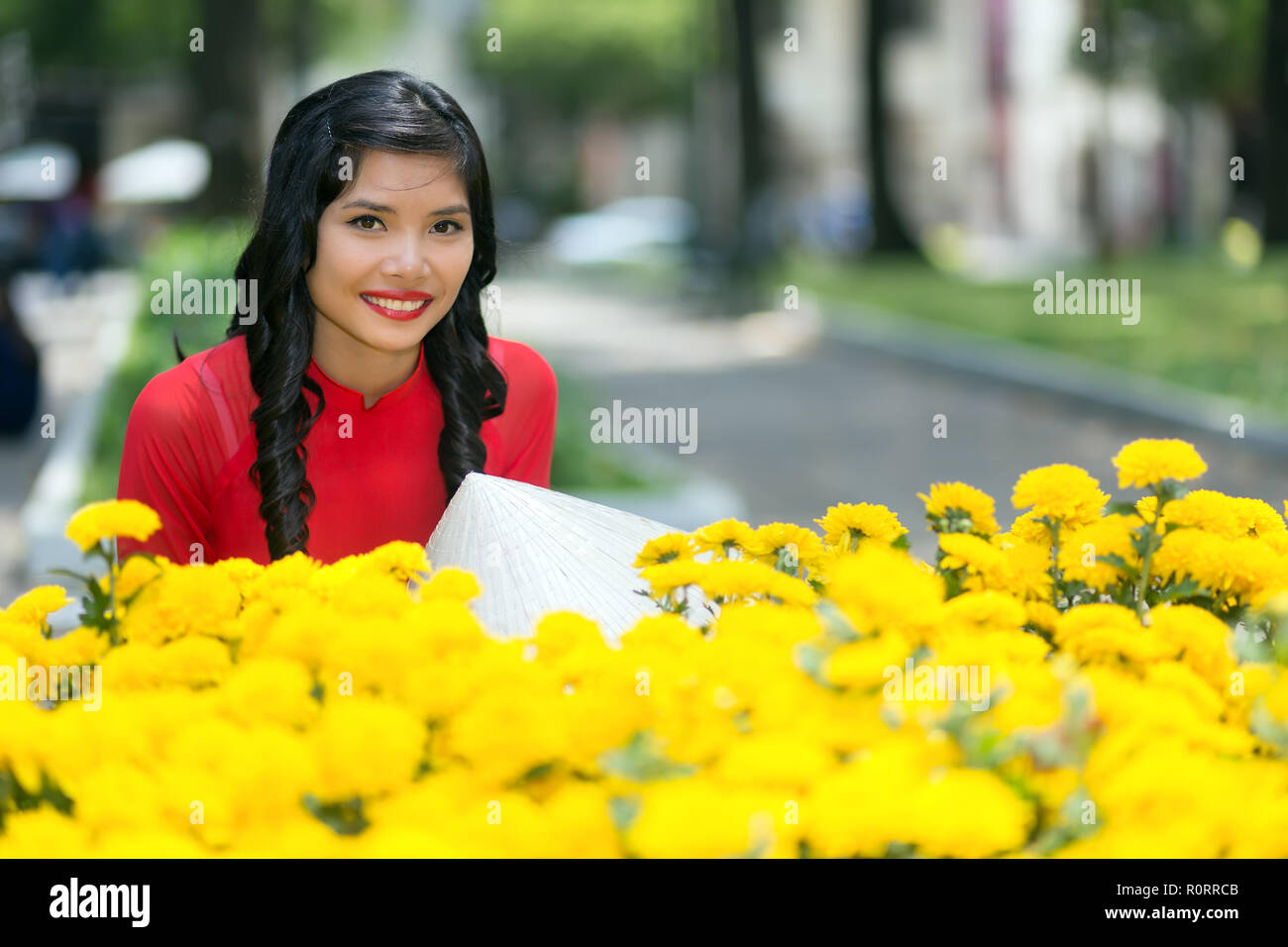 Attraente giovane vietnamita donna sorridente felicemente con la videocamera su un display di fiori gialli in una strada urbana Foto Stock