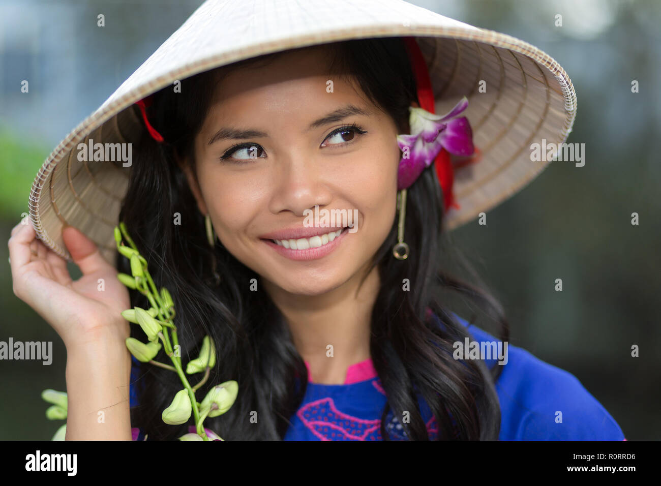 Piuttosto il vietnamita donna che indossa un tradizionale cappello conico con un fiore nei suoi capelli sorridendo felicemente come si guarda in aria Foto Stock