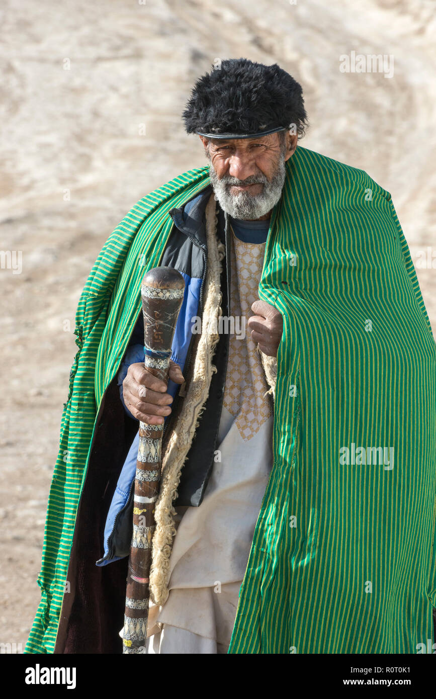 Il vecchio uomo sufi indossano manto verde a piedi nel deserto con bastone verso l'hashish fumatori Den, Old Balkh, Nord Afghanistan Foto Stock