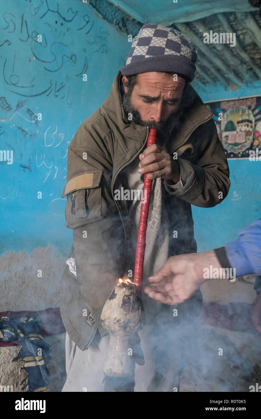 Uomo di fumare hashish con un bong vicino alla tomba di un santo Sufi, antica Balkh, Nord Afghanistan Foto Stock