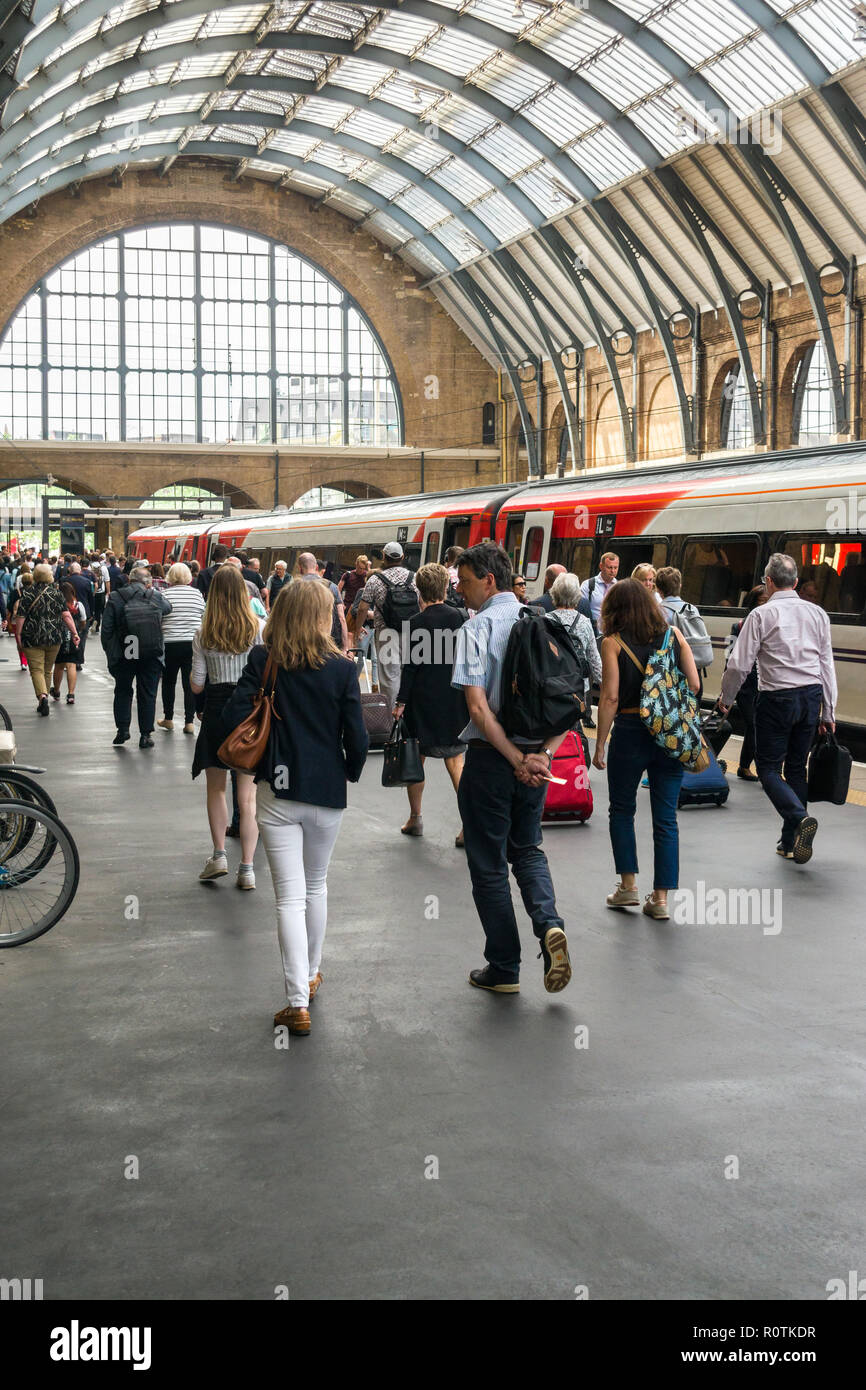 Pendolari camminare davanti a un treno in una piattaforma nella stazione di King Cross su una soleggiata giornata estiva, London, Regno Unito Foto Stock